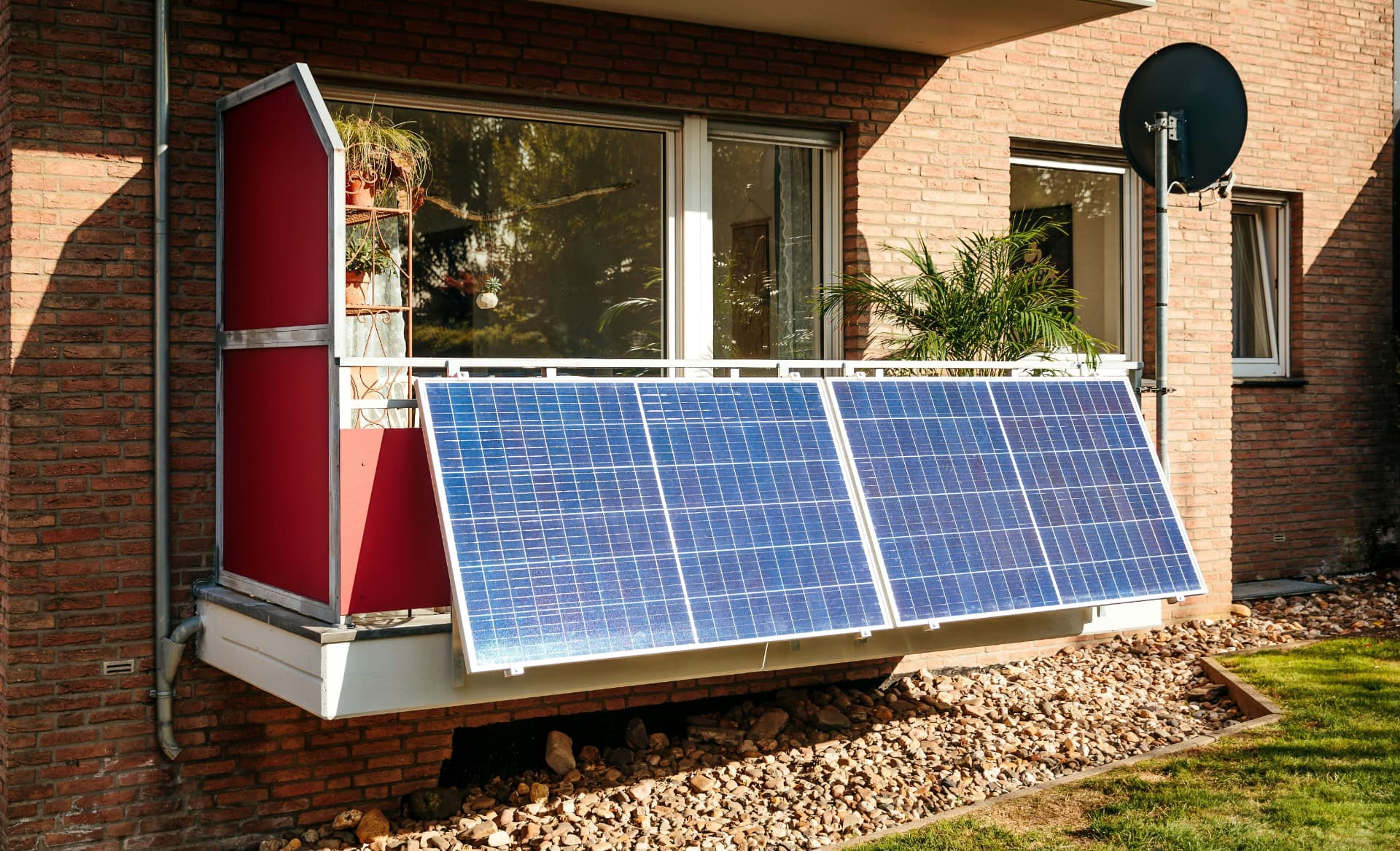 Four plug-in solar panels mounted along the outside of an apartment balcony railing, tilted toward the sun
